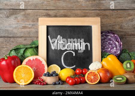 Diversi prodotti e lavagna con frase VITAMINA C su tavola di legno Foto Stock