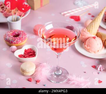 Tavolo romantico dolce con bicchiere di vino rosa, waffle, ciambella, gelato, macaron, lollipop, caramelle. Il concetto di San Valentino. Foto Stock