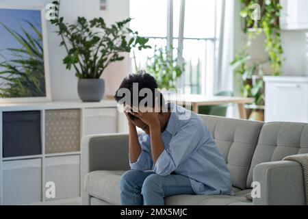 Depressa esaurita infelice giovane donna si siede sul divano casa nascondendo faccia in mani si sentono ingannati da soli. Foto Stock