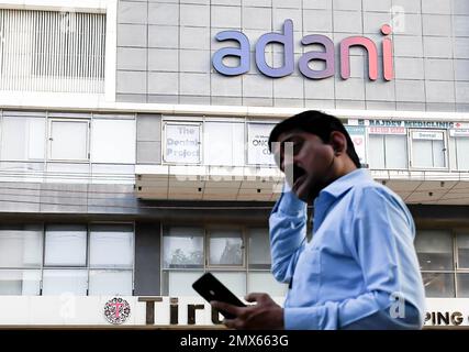 Un uomo controlla il suo cellulare mentre cammina accanto al logo Adani sulla costruzione a Mumbai. Adani ha annullato la sua offerta pubblica di follow-on (FPO) un giorno dopo che è stata pienamente sottoscritta. In una dichiarazione la società ha dichiarato di avere richiamato l'offerta pubblica di follow-on (FPO) a causa della volatilità del mercato e restituirà il denaro agli investitori. Foto Stock