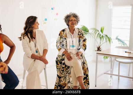 Diverse donne d'affari sorridono felicemente durante una conferenza in un ambiente di lavoro moderno. Gruppo di donne d'affari riuscite che lavorano insieme in un tutto- Foto Stock