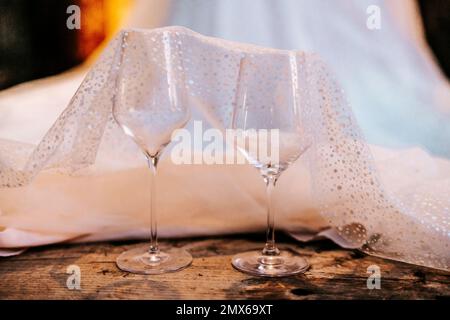 Due bicchieri da vino disposti con abito da sposa su pavimento in legno Foto Stock