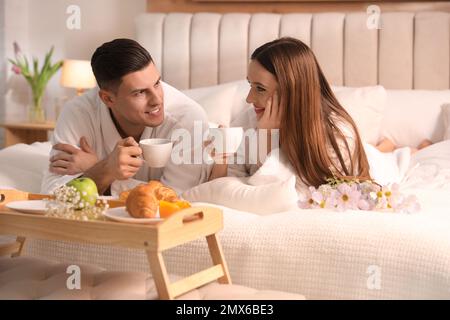 Coppia felice in accappatoi facendo colazione a letto a casa Foto Stock