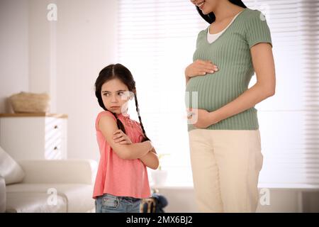 Bambina infelice vicino a madre incinta a casa. Sentirsi gelosi verso il fratello nascituro Foto Stock