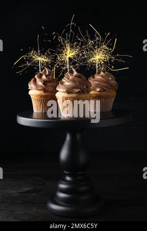 Cupcake di compleanno con scintillanti in piedi su sfondo scuro Foto Stock