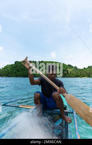 Foto verticale filippino pescatore file su una piccola barca andare a pesca con la rete di pesca su un'isola tropicale. persone reali Foto Stock