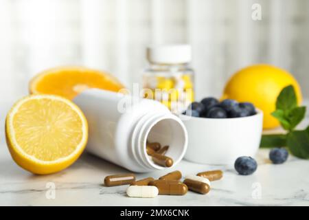 Bottiglia con pillole vitaminiche, mirtilli e limone su tavolo di marmo bianco Foto Stock