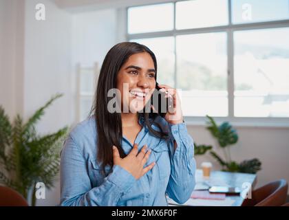 Giovane donna d'affari indiana tiene mano a cuore durante la chiamata telefonica in ufficio Foto Stock