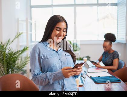 Giovane donna d'affari che usa il cellulare, collega nello spazio ufficio della sala riunioni Foto Stock