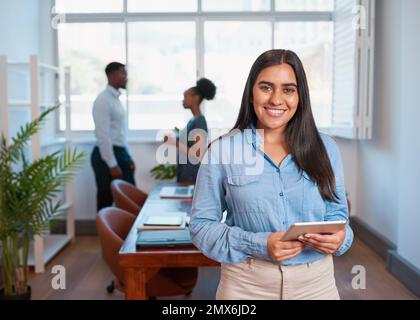 Una giovane e attraente donna in viaggio d'affari è in piedi con un tablet nella sala riunioni dell'ufficio Foto Stock