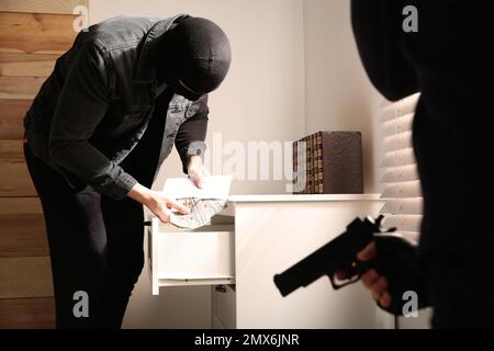Criminali mascherati pericolosi con armi che rubano denaro dalla casa Foto Stock