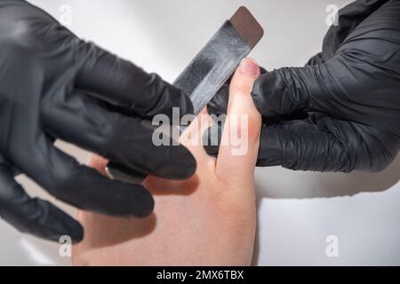 Mani gloved di un manicurist esperto che archivano le unghie di una donna giovane con una lima del chiodo. Mani durante una sessione di cura manicure in un salone di spa. Manicurista fi Foto Stock