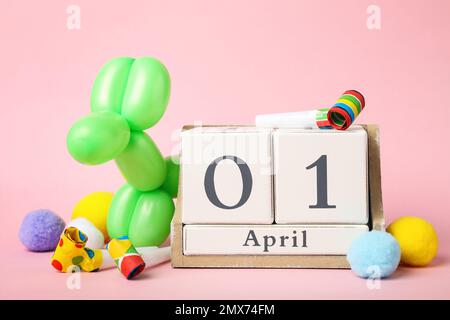 Calendario in legno e decorazioni per feste su sfondo rosa. Aprile Fool's Day Foto Stock