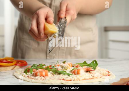 Donna grattugiare il formaggio su pizza a tavola di marmo bianco, primo piano Foto Stock