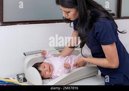 Pediatra che posa un bambino sulla bilancia nel suo ufficio per la pesatura. Foto Stock