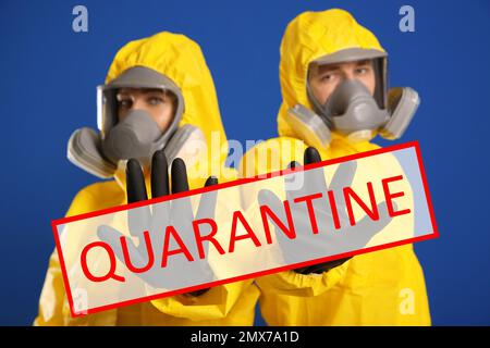 Quarantena durante l'epidemia di coronavirus. Uomo e donna in tute di protezione chimica facendo un gesto di arresto su sfondo blu Foto Stock