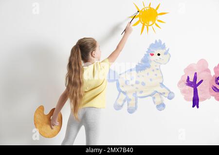 Bambino piccolo disegno unicorno su parete bianca all'interno Foto Stock