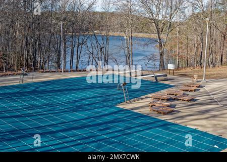 Chiuso per la stagione una piscina pubblica in un parco con una copertura sull'acqua con sedie e lettini ancora che circondano la grande piscina vista parziale dal Th Foto Stock