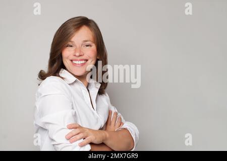 Ritratto di felice sorridente medico felice in uniforme bianco cappotto in piedi con mani incrociate su sfondo grigio parete Foto Stock