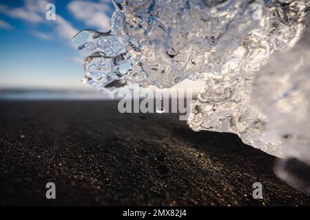 Fuoco selettivo di goccia di acqua che gocciola dal pezzo trasparente di ghiaccio che fonde alla luce del sole su Seacoast in Islanda Foto Stock