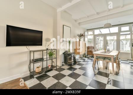 All'interno di una moderna e spaziosa sala da pranzo con tavolo e sedie vicino a mensole e TV appesa a parete Foto Stock