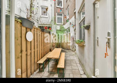 Tavolo in legno e panchine poste vicino recinzione con piante in vaso in cortile fuori casa residenziale Foto Stock