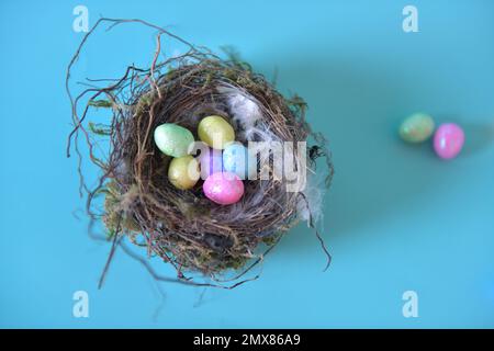 Vista dall'alto dei nidi di uccelli reali pieni di uova di Pasqua artificiali in più colori. Due uova in più sullo sfondo. Foto Stock