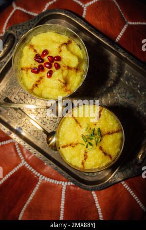 Due porzioni di Zarda Sholeh, un budino di riso allo zafferano persiano, dessert con cannella, melograno e guarnitura al pistacchio Foto Stock
