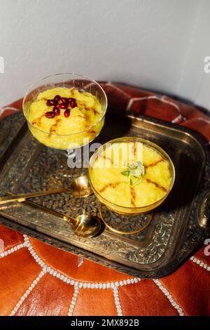 Due porzioni di Zarda Sholeh, un budino di riso allo zafferano persiano, dessert con cannella, melograno e guarnitura al pistacchio Foto Stock