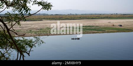 Un'unica barca da pesca viaggia lungo il fiume Irrawaddy al sole di mezzogiorno in Myanmar (Birmania). Foto Stock