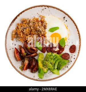 Deliziosa colazione a base di grano saraceno, pomodori secchi al sole, avocado, uova fritte con basilico e salsicce da caccia Foto Stock