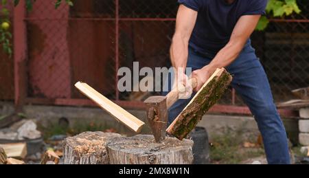 Un lumberjack con un'ascia pesante in mano sta tritando la legna da ardere. Un'ascia nelle mani di un uomo. il tronco si frantumò in pezzi. Foto Stock