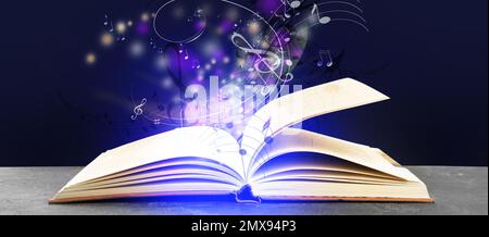 Sinfonia splendente con note musicali da libro aperto su tavolo su sfondo viola scuro. Design del banner Foto Stock