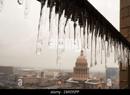 Austin Texas USA, febbraio 1 2023: I ghiaccioli sgocciolano da un balcone con il Campidoglio del Texas sullo sfondo come Austin e il Texas centrale recuperare da una tempesta di ghiaccio che ha abbattuto il potere a migliaia e ha causato danni agli alberi in tutta la città. Circa un terzo di Austin è senza potere due giorni dopo la tempesta colpito. Credit: Bob Daemmrich/Alamy Live News Foto Stock