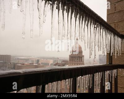 Austin Texas USA, febbraio 1 2023: I ghiaccioli sgocciolano da un balcone con il Campidoglio del Texas sullo sfondo come Austin e il Texas centrale recuperare da una tempesta di ghiaccio che ha abbattuto il potere a migliaia e ha causato danni agli alberi in tutta la città. Circa un terzo di Austin è senza potere due giorni dopo la tempesta colpito. Credit: Bob Daemmrich/Alamy Live News Foto Stock