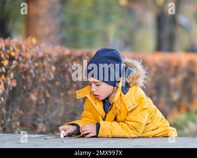 Il bambino scrive o disegna qualcosa con il gesso sul marciapiede. Attività ricreative creative all'aperto in autunno. Foto Stock