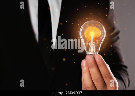 Uomo che tiene lampadina con cervello splendente all'interno contro sfondo grigio, primo piano. Generazione di idee Foto Stock