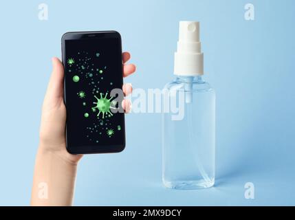 Sanificazione dei dispositivi mobili durante l'epidemia di coronavirus. Antisettico spray e donna con smartphone su sfondo blu, primo piano Foto Stock