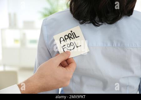 Uomo che si attacca APRILE SCIOCCO nota alla schiena del collega in ufficio, primo piano Foto Stock