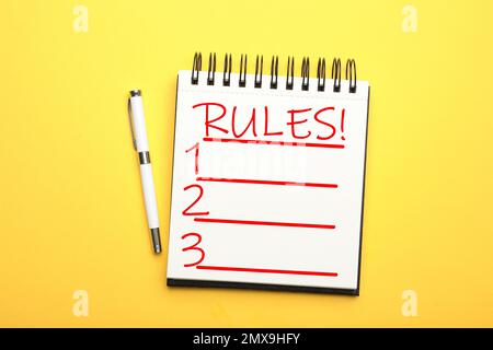 Quaderno con lista di regole e penna su sfondo giallo, piatto Foto Stock