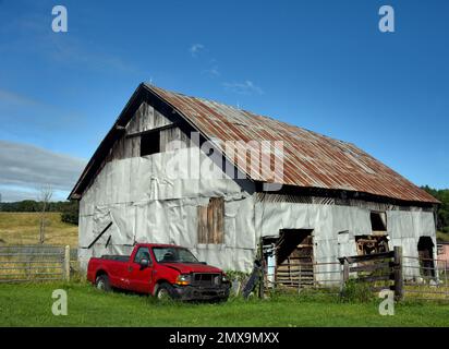 Vecchio fienile di legno, con tetto di latta, è tenuto insieme con latta di scarto. Il camion sommerso siede accanto al granaio. Foto Stock