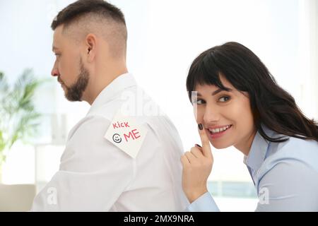 Una giovane donna che si attacca MI DÀ un'annotazione alla schiena del collega in carica. Aprile Fool's Day Foto Stock