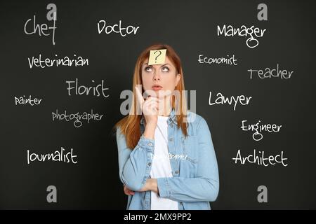 Donna premurosa con adesivo punto interrogativo sulla fronte scegliendo professione contro sfondo scuro Foto Stock