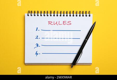 Notebook con elenco di regole e penna su sfondo giallo, vista dall'alto Foto Stock