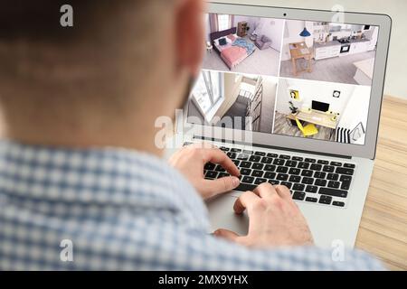 Uomo che controlla le telecamere cctv moderne su laptop indoor, closeup. Sistema di sicurezza domestica Foto Stock