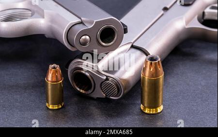 Due pistole in acciaio inox 1911, una a 45 ACP e l'altra di calibro 380 con un proiettile a punta cava per ciascuna di esse su fondo nero Foto Stock
