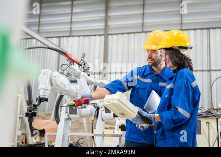 Un team di ingegneri maschili e femminili si riunisce per ispezionare i robot di saldatura dell'acciaio controllati dal computer. Pianificare le prove e l'installazione per l'uso. Foto Stock