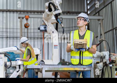 Un team di ingegneri maschili e femminili si riunisce per ispezionare i robot di saldatura dell'acciaio controllati dal computer. Pianificare le prove e l'installazione per l'uso. Foto Stock