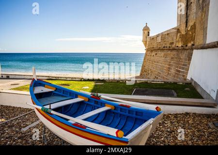 La tradizionale barca in legno e la Fortezza di San Giacomo sulla spiaggia di Sesimbra, Area Metropolitana di Lisbona, Portogallo Foto Stock