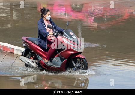 SAMUT PRAKAN, THAILANDIA, 25 2023 GENNAIO, Una donna con maschera facciale cavalca una moto attraverso pozza Foto Stock